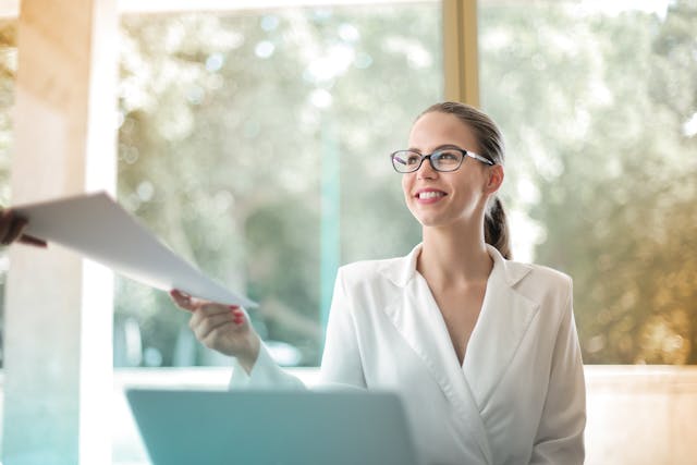 a person smiling at their desk while being handed documents