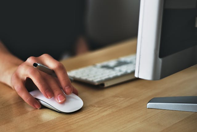 a hand holding a pen while also using a computer mouse