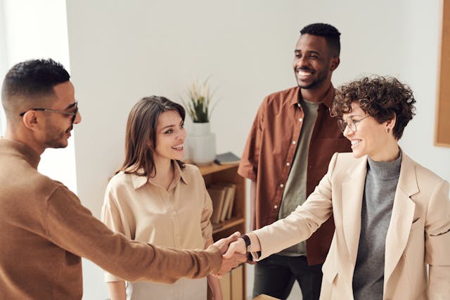 four people talking while two shake hands