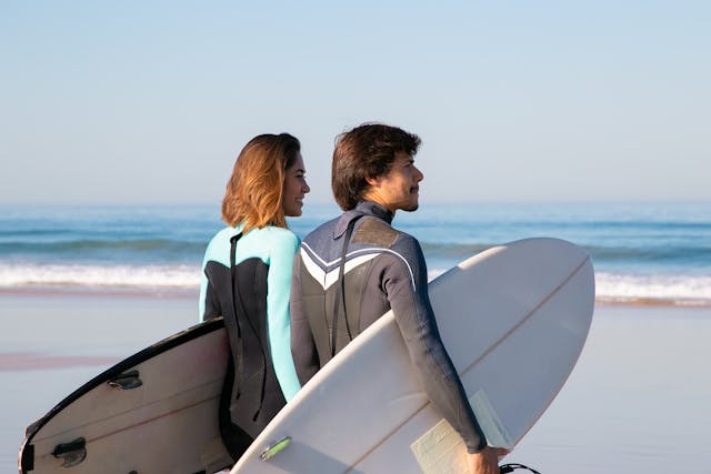 two people standing on beach holding surfboards