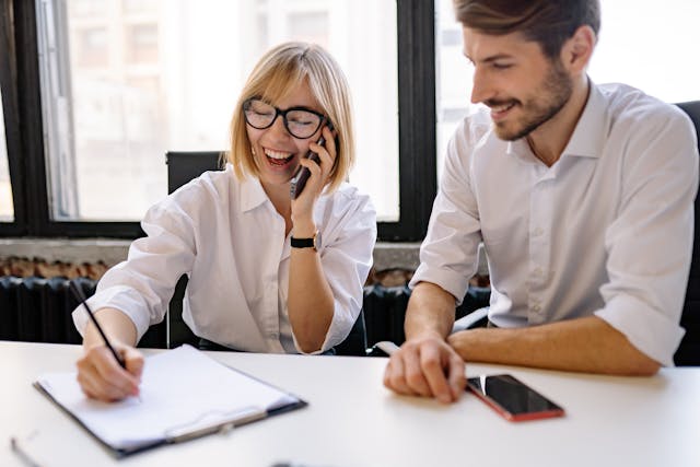 a person talking on the phone and taking notes with someone next to them