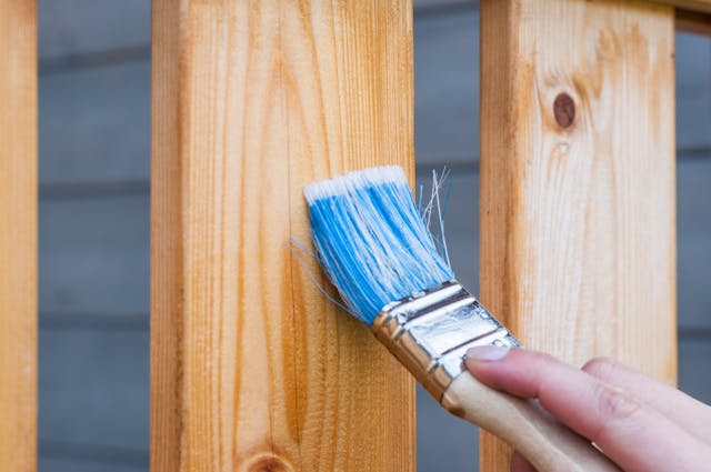 a paint brush applying wood stain to a deck