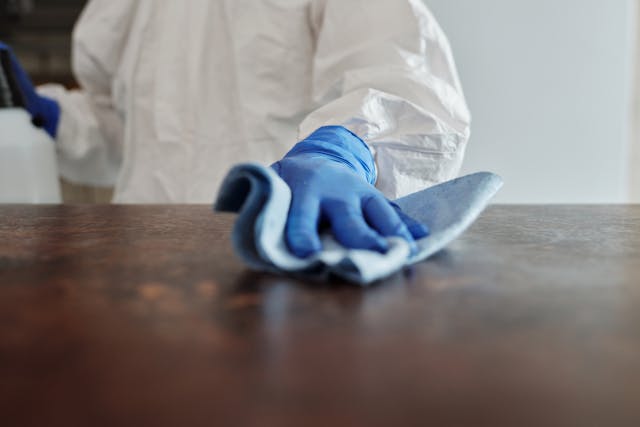 person in coveralls and blue gloves cleaning a surface