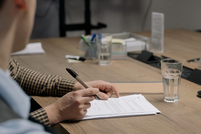 person sitting at a desk looking over a document while holding a pen about to sign it