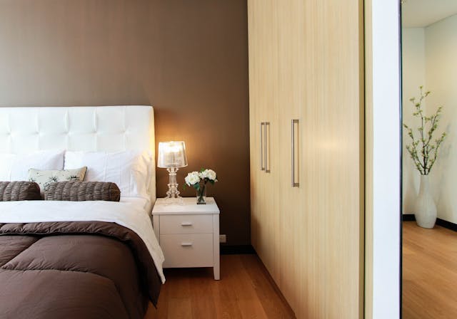 a bed with brown and white bedding and lightwood storage units