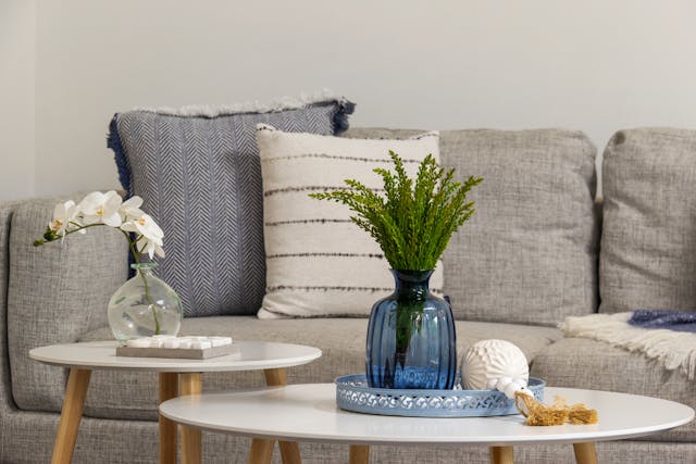 a grey linen couch with woven throw pillows a white and light wood coffee table