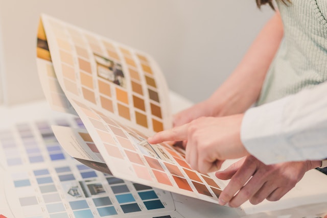 hand pointing to a paint sample on a paper covered in color swatches